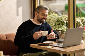 Obraz premium Mature man enjoying coffee at a cozy cafe while working on his laptop