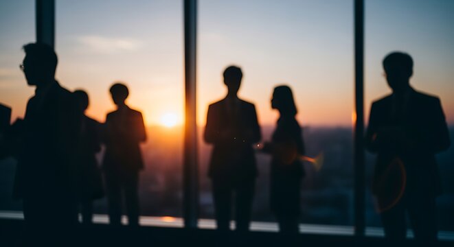 Silhouettes of business people observing a sunset from a high-rise office building, symbolizing success and contemplation