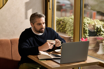 Mature man enjoying coffee while working on a laptop in a cozy cafe setting