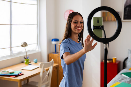 Young teenage girl is adjusting smartphone before filming videos in her cozy room. Content creator, adolescence and digital generation concept.