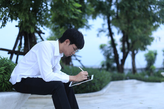 Focused new employee for small business working remotely in park. young asian man drawing on digital tablet