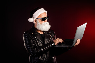Rocker Santa in leather jacket using a laptop with beard and sunglass for festive Christmas theme a modern quirky holiday stock photo