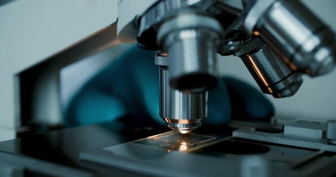 Detailed macro of gloved hands adjusting laboratory microscope for analysis