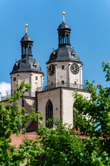 Obraz premium Towers of St. Mary’s Church in Wittenberg peeking out from behind trees. Historic Reformation church linked to Martin Luther.