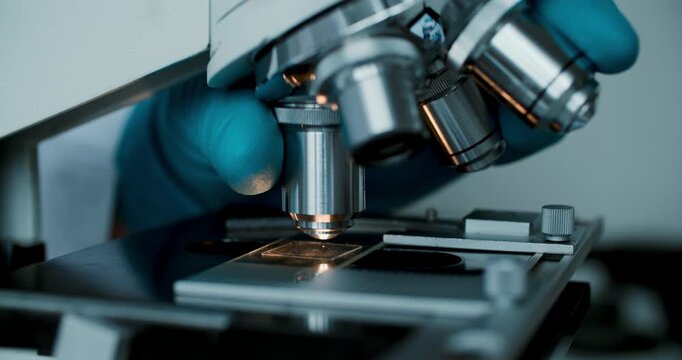 Detailed macro of gloved hands adjusting laboratory microscope for analysis