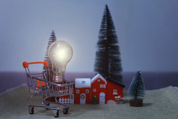 Hopeful concept of glowing light bulb in shopping cart near house, symbolizing home energy and...