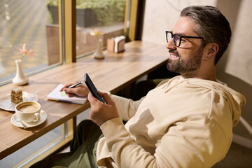 Mature man in stylish attire enjoys coffee while writing notes at a cozy café