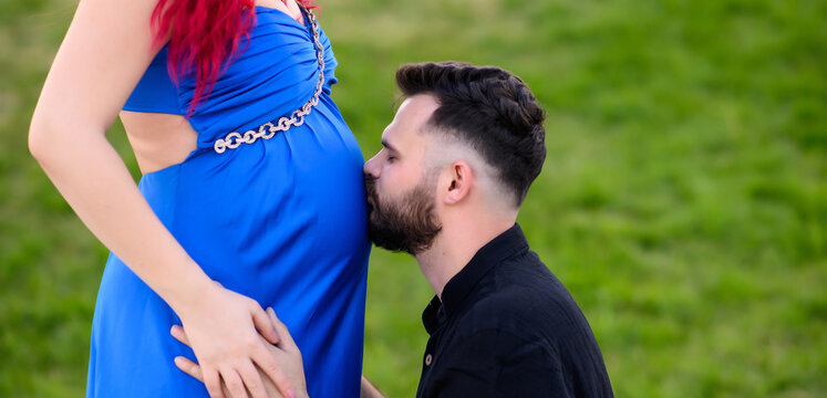A man gently kisses a pregnant woman’s belly in a blue dress, touching it with his hands. A tender moment of expecting a baby, filled with love and warmth