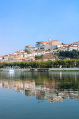 A scenic view of Coimbra, Portugal, capturing the historic University of Coimbra and the city’s hillside architecture reflected on the calm waters of the Mondego River