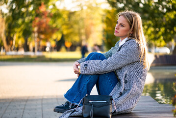 Portrait of sad businesswoman sitting alone on a park bench in the city during autumn day.