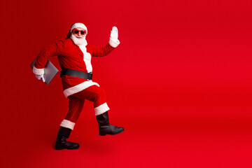 Santa in red costume with hat and beard waves on red background for christmas stock photo featuring festive character