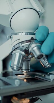 Detailed macro of gloved hands adjusting laboratory microscope for analysis