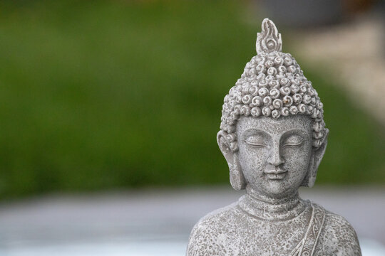 Close-up of a grey stone Buddha statue head in a peaceful garden with green background
