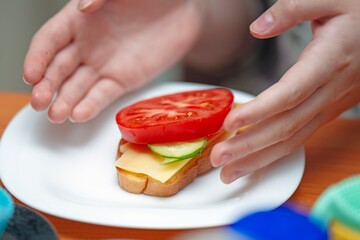 Teenager preparing to eat a homemade sandwich with bread, cheese, cucumber, and tomato