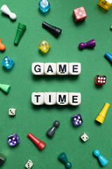 Wooden dice show the phrase 'Game Time' with a selection of colourful dice and game tokens lying around it on a vibrant green baize fabric