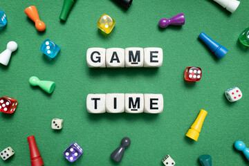 Wooden dice show 'Game Time' with a selection of colourful dice and game tokens lying around it on a vibrant green baize fabric