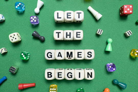 Wooden dice show the phrase 'Let The Games Begin' with a selection of colourful dice and game tokens lying around it on a vibrant green baize fabric