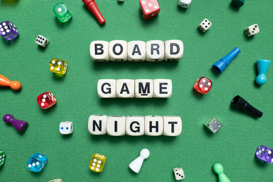 Wooden dice showing 'Board Game Night' with a selection of colourful dice and game tokens lying around it on a vibrant green baize fabric - Powered by Adobe