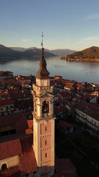 Cinematic drone flight over Lake Como framed by autumn-winter mountains and a red-tiled Italian village, with a tall historic bell tower rising above the rooftops