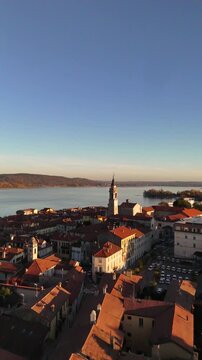 Cinematic drone flight over Lake Como framed by autumn-winter mountains and a red-tiled Italian village, with a tall historic bell tower rising above the rooftops
