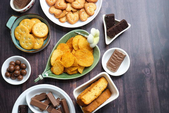 Assorted party snacks on table featuring chocolate cream sandwich biscuits, sugar coated heart cookies, wafer chocolates, chocolate coated caramel balls, salted crackers, and crispy potato chips.