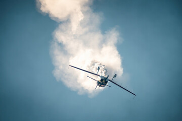 Aerobatic plane flying vertically downward creating a spectacular spiral of white smoke during an airshow against clear blue sky.