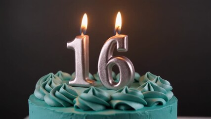 Close-up of a turquoise cake decorated with swirl frosting and lit silver birthday candles in the shape of the number 16