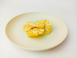 Keripik Tempe or Tempeh Chips on a round plate, isolated on white background. Traditional Indonesian food are made from soybeans mixed with rice flour then sliced ​​thinly.