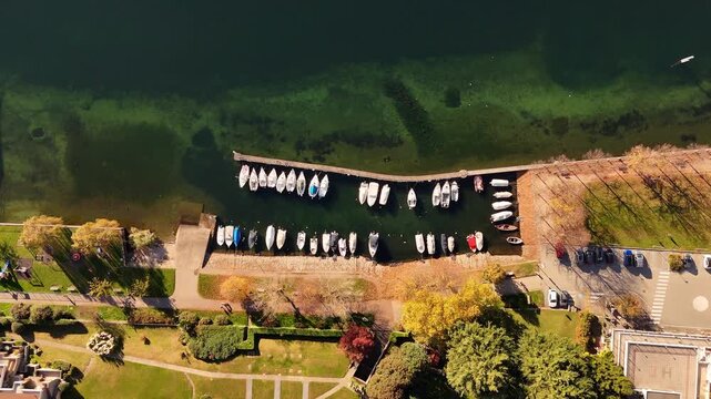 Aerial drone flight over a marina on Lake Como with boats moored along the waterfront, surrounded by alpine scenery and reflective waters in a cinematic lakeside view