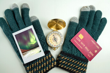 Instant print of the view of the aurora and winter gloves with a credit card and compass on a white background. Concept of finance and travel