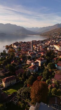 Cinematic drone flight over Lake Como framed by autumn-winter mountains and a red-tiled Italian village, with a tall historic bell tower rising above the rooftops