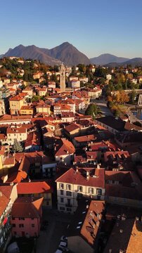 Cinematic drone flight over Lake Como framed by autumn-winter mountains and a red-tiled Italian village, with a tall historic bell tower rising above the rooftops