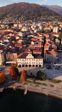 Cinematic aerial orbit of a Lake Maggiore village with red rooftops, autumn mountains and serene lakeside views, capturing the warm and atmospheric essence of northern Italy