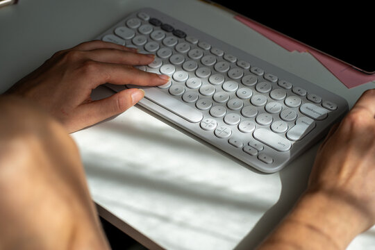 Hands typing on modern wireless keyboard on white desk - Powered by Adobe