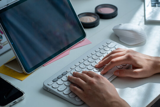 Hands typing on wireless keyboard, tablet and mouse on white workspace