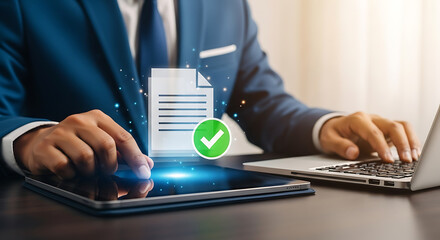 Businessman uses tablet and laptop for document approval with a green check mark, showcasing successful project management and task completion.