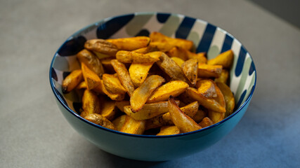Golden baked potato wedges in patterned bowl on counter