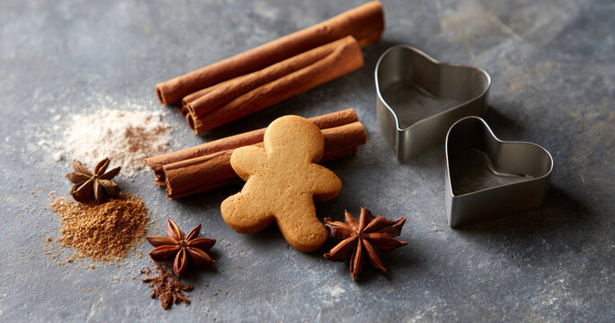 Gingerbread cookie with cinnamon sticks, star anise, and heart-shaped cookie cutters on textured surface - Powered by Adobe