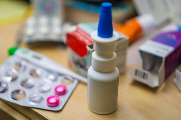 closeup of a nasal spray bottle and various pills on a wooden table concept of cold and flu...