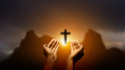 Human hand raising and praying with the Christian cross on the hill with dark dramatic sky background. Concept of Christianity, religious, faith, Jesus, or belief