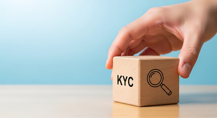 Hand holding wooden block with KYC and magnifying glass symbol against a blue background, representing identity verification and regulatory compliance