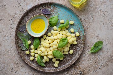 Plate with raw italian chicche di patate, olive oil and basil on a beige granite background, horizontal shot, view from above