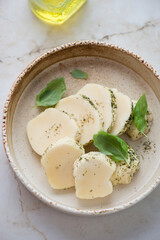 Bowl with sliced halloumi cheese and herbs, vertical shot on a light-beige marble background, elevated view, middle close-up