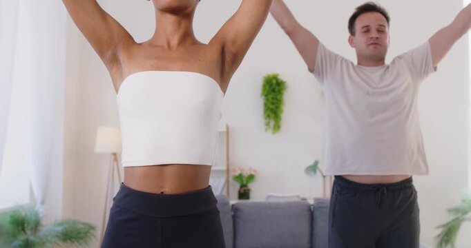 Couple practicing yoga fitness stretching exercise at home. Partners raise arms upward, focus on breathing, meditation, and sport workout. Peaceful teamwork, wellness and healthy lifestyle.