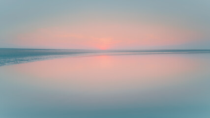 Calm water reflects a fading sunset on a wide, flat beach, with a low horizon line.