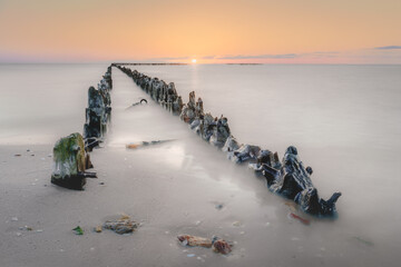 Serene beauty of a sunset seascape, where weathered wooden groynes stretch into calm waters, captured with a long exposure for a dreamlike motion blur.