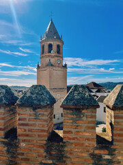 Church tower under blue sky seen from behind brick defense wall. Velez-Malaga, Malaga, Spain.