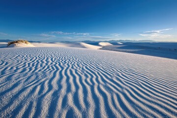 Wind-sculpted ripples on white gypsum dunes under a clear blue sky