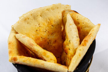 Foccacia or pita. Triangular pieces of lightly browned Pita, Naan, or flatbread served in a black fabric basket on a white background.