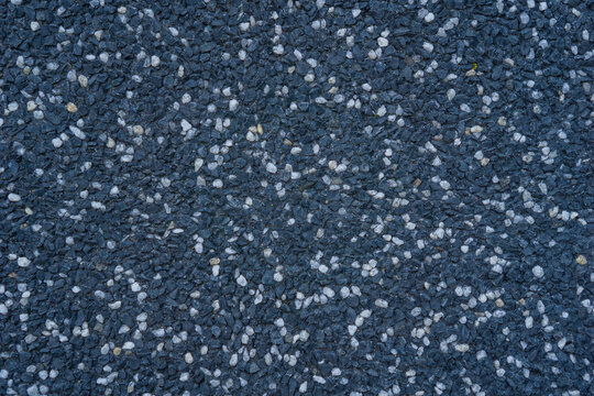 dark blue-grey exposed aggregate surface texture with scattered white and grey pebbles, detailed uniform construction background, concept of building material, flooring, urban design